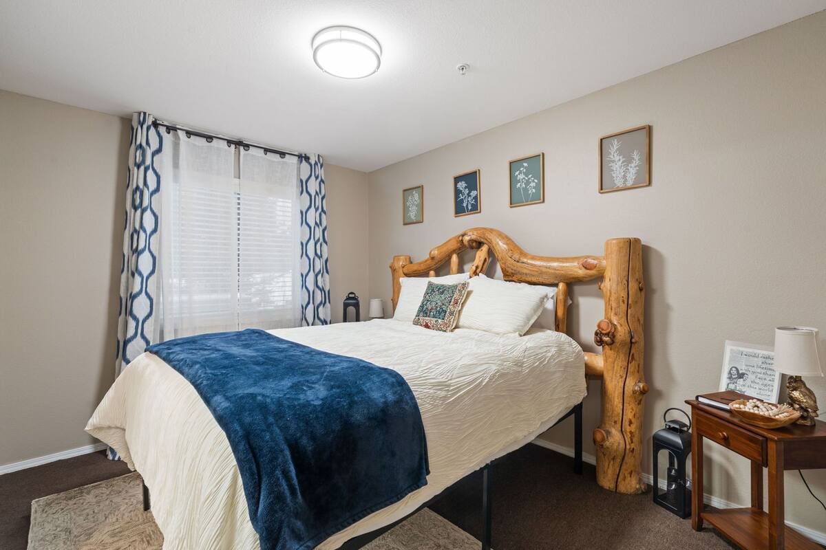 A bedroom with a bed, a wooden headboard, a nightstand, a lamp, and framed pictures on the wall.