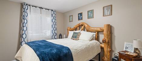 A bedroom with a bed, a wooden headboard, a nightstand, a lamp, and framed pictures on the wall.