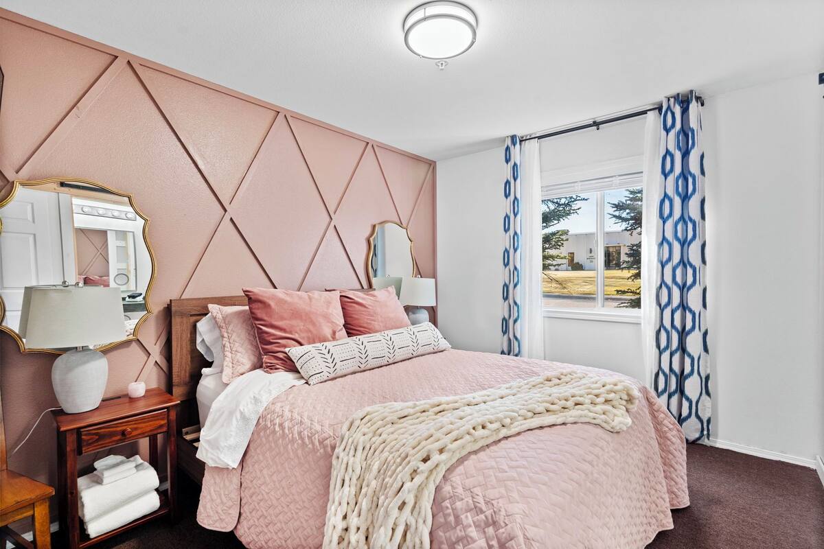 A bedroom with a bed, bedside tables, a mirror, and a window with patterned curtains.