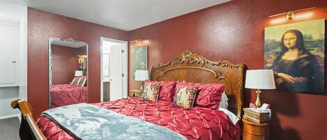 A bedroom with a wooden bed, red and blue bedding, a mirror, a dresser, and a painting of the Mona Lisa.