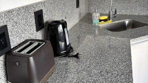 Une cuisine dotée d’un plan de travail en granit, d’un grille-pain, d’une machine à café, d’un évier avec un robinet et d’une fenêtre située au-dessus de l’évier.