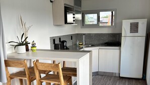 Une cuisine moderne dotée d’un îlot central, de chaises en bois, d’un réfrigérateur et d’une fenêtre laissant entrer la lumière naturelle.