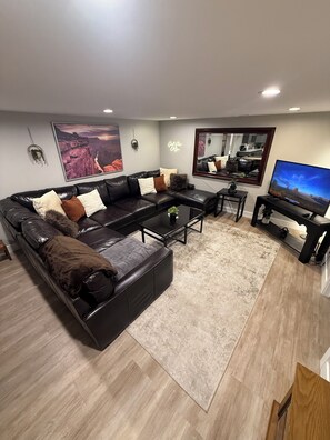 A modern living room with a sectional sofa, a coffee table, a TV, and a large framed picture on the wall. - 7BR Retreat - Hot Tub • Fire Pit • 2 King Suites • Near SLC (Sandy)