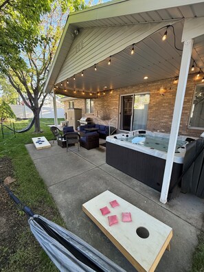Un patio couvert avec des sièges d’extérieur, un jacuzzi et une table en bois agrémentée de coussins roses.