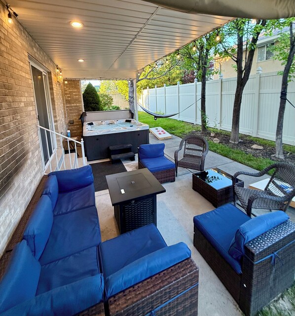 A covered patio area with outdoor furniture, a hot tub, and a view of the backyard.