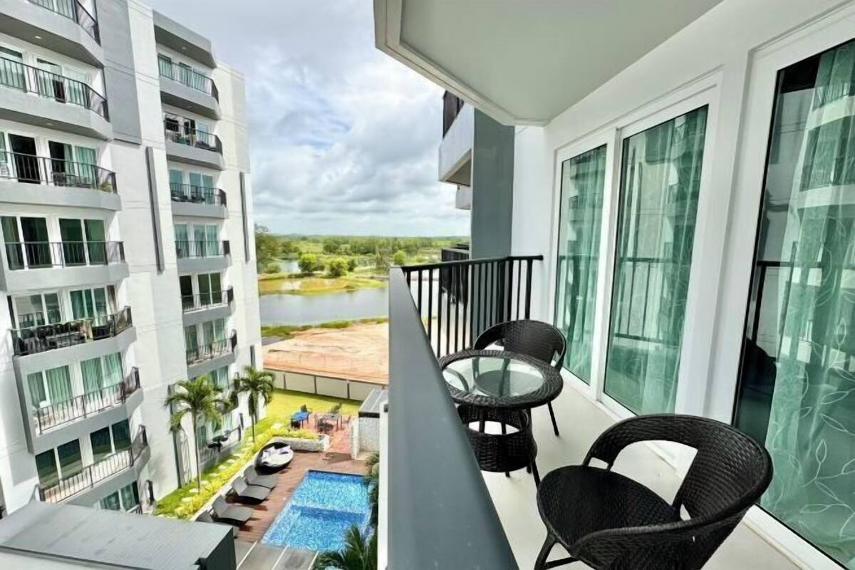 A balcony with a view of a river, a pool, and a building with multiple balconies.