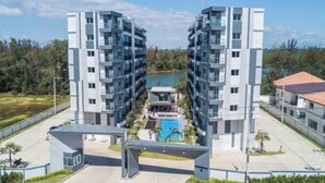 A modern apartment complex with a central courtyard featuring a swimming pool, surrounded by greenery and a clear sky.