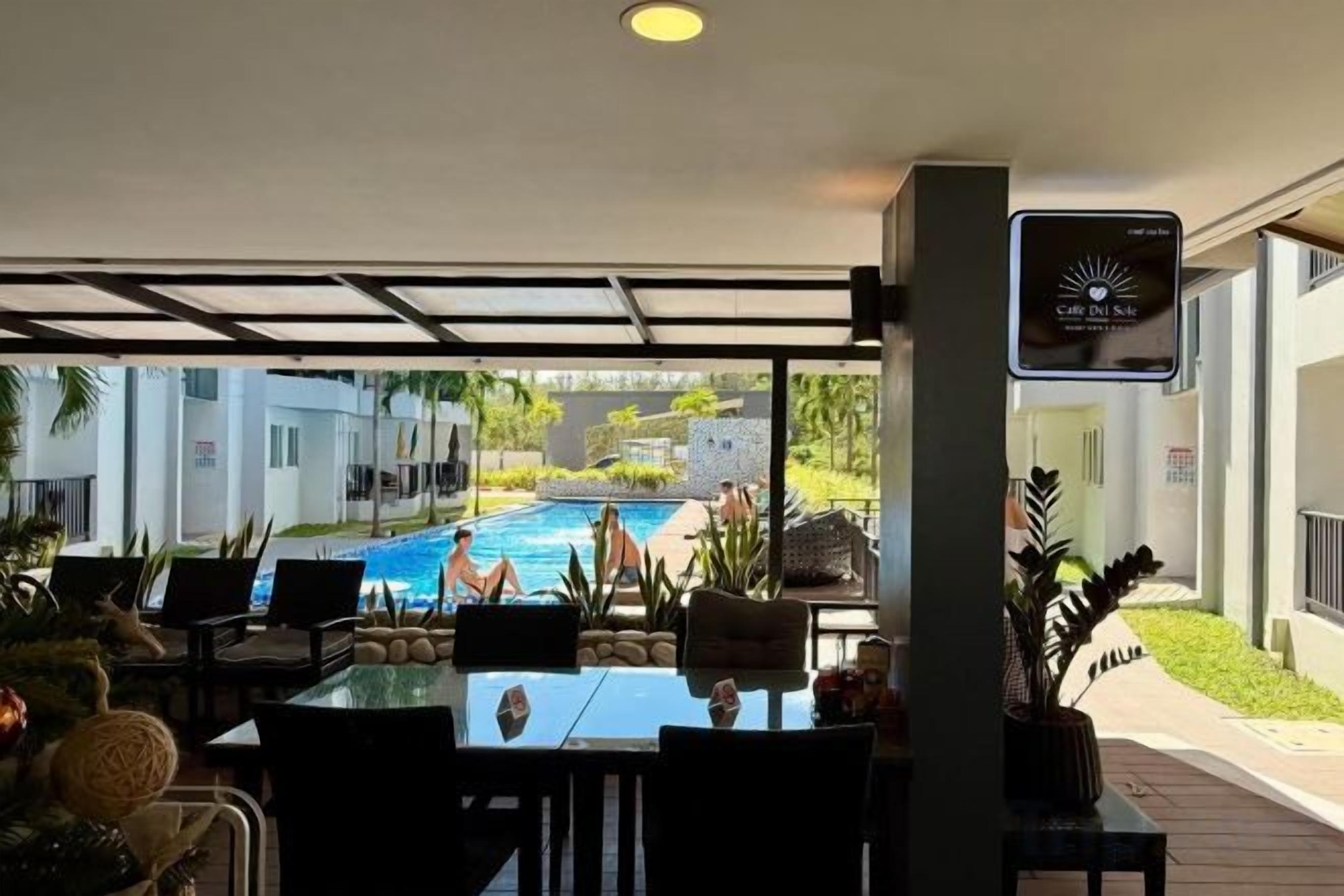Un área de estar al aire libre techada con vista a la piscina, una pantalla digital y una planta en maceta.