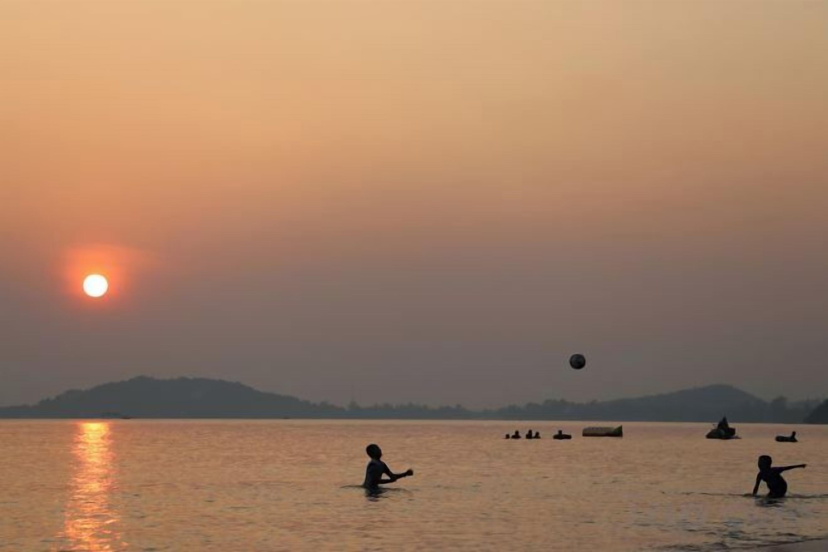 Atardecer sobre un cuerpo de agua con barcos y gente.