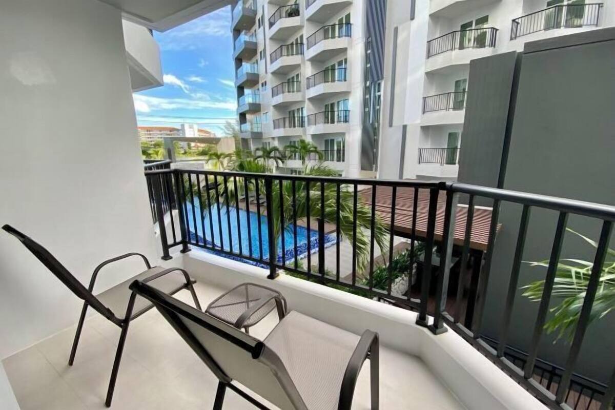 A balcony with a pool view, a chair, and a building with balconies.