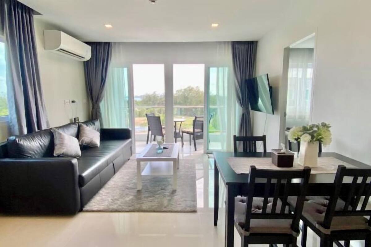 A modern living room with a sofa, coffee table, dining table, chairs, and a flat-screen TV.