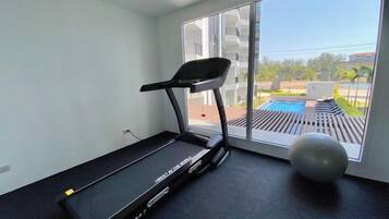 Una habitación con una cinta de correr, un ventanal y vista a una piscina.