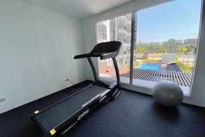 A room with a treadmill, a large window, and a view of a swimming pool. - Mantra Beach Condominium MaePhim - 2 (Klaeng)