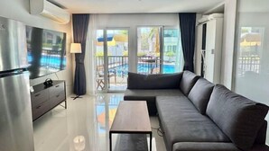 A modern living room with a sofa, a coffee table, a TV, and a balcony with a pool view.