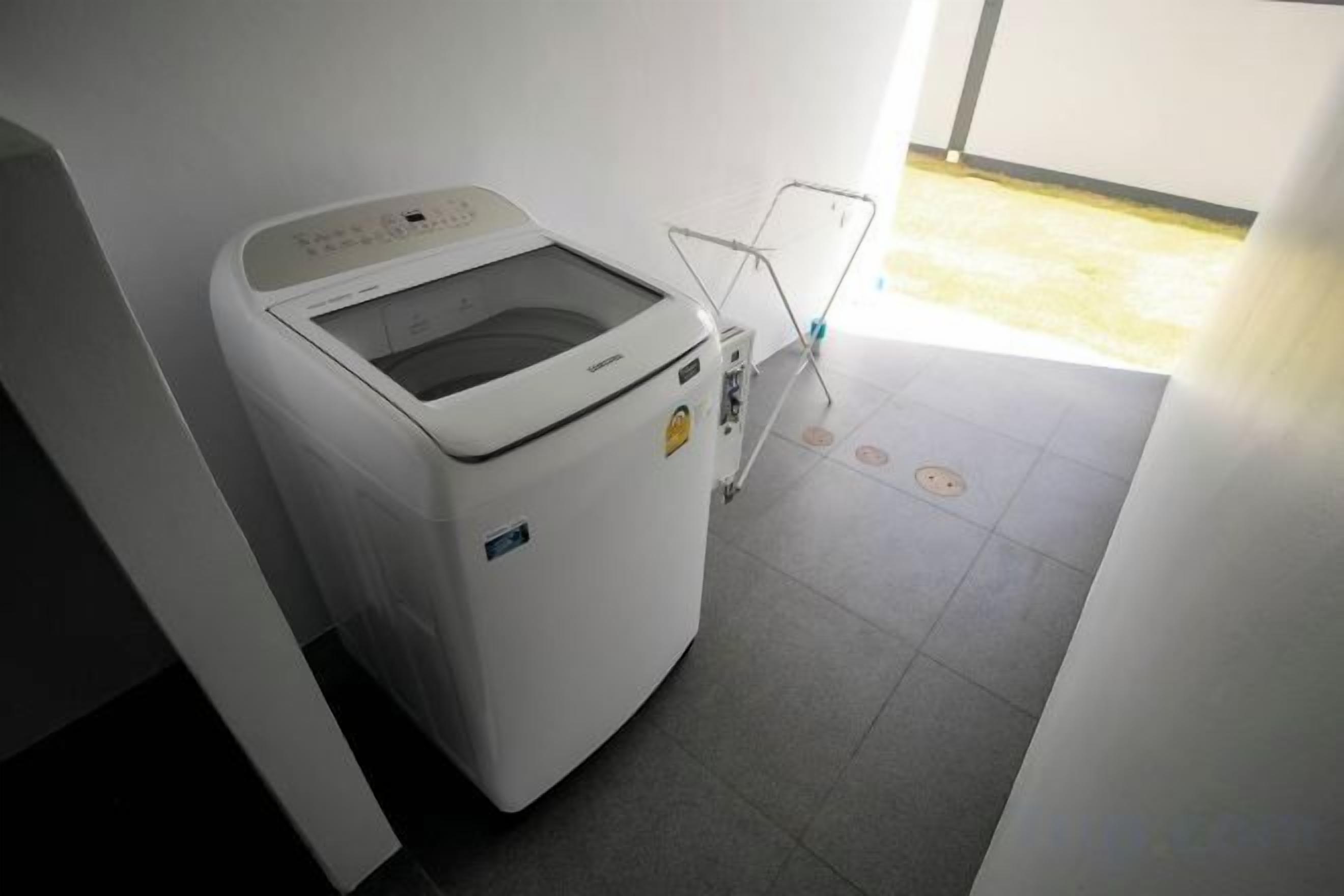 Una lavadora blanca en una habitación con piso de baldosas y una puerta que da a un área exterior.