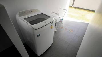 Una lavadora blanca en una habitación con piso de baldosas y una puerta que da a un área exterior.