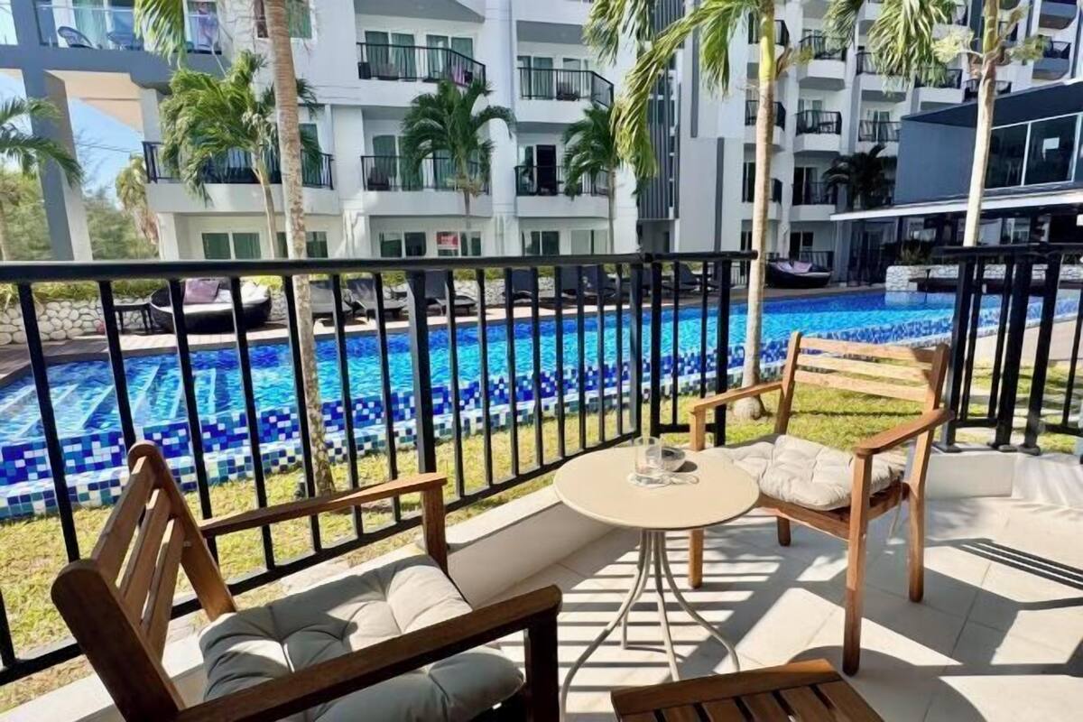 A balcony with a pool view, wooden furniture, and a building in the background.