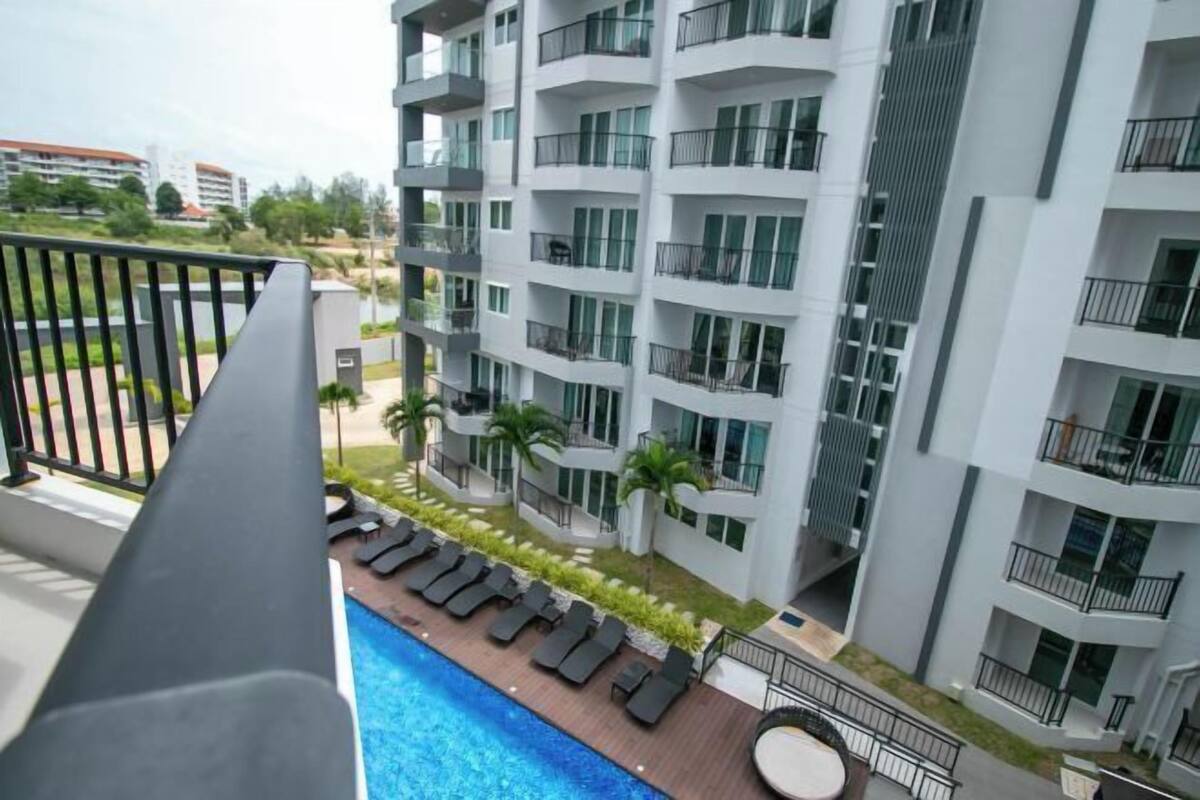 A modern multi-story hotel with balconies, a swimming pool, and a landscaped garden area.
