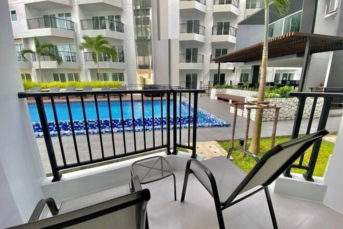 A balcony with a pool view, outdoor seating, and a modern building in the background.