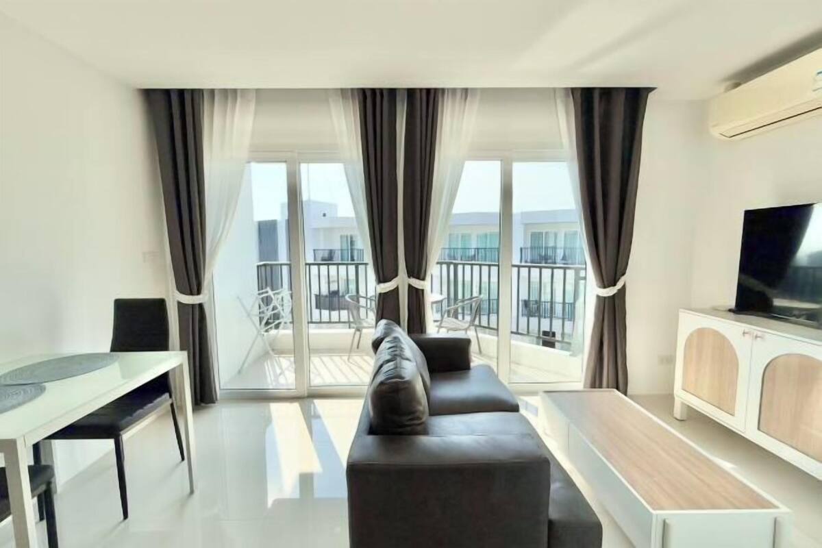 A modern living room with a sofa, TV, dining table, and balcony view.
