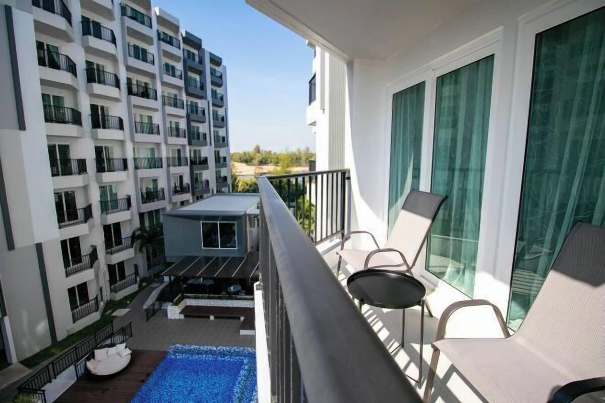 A balcony with a pool, chairs, and a view of adjacent buildings.