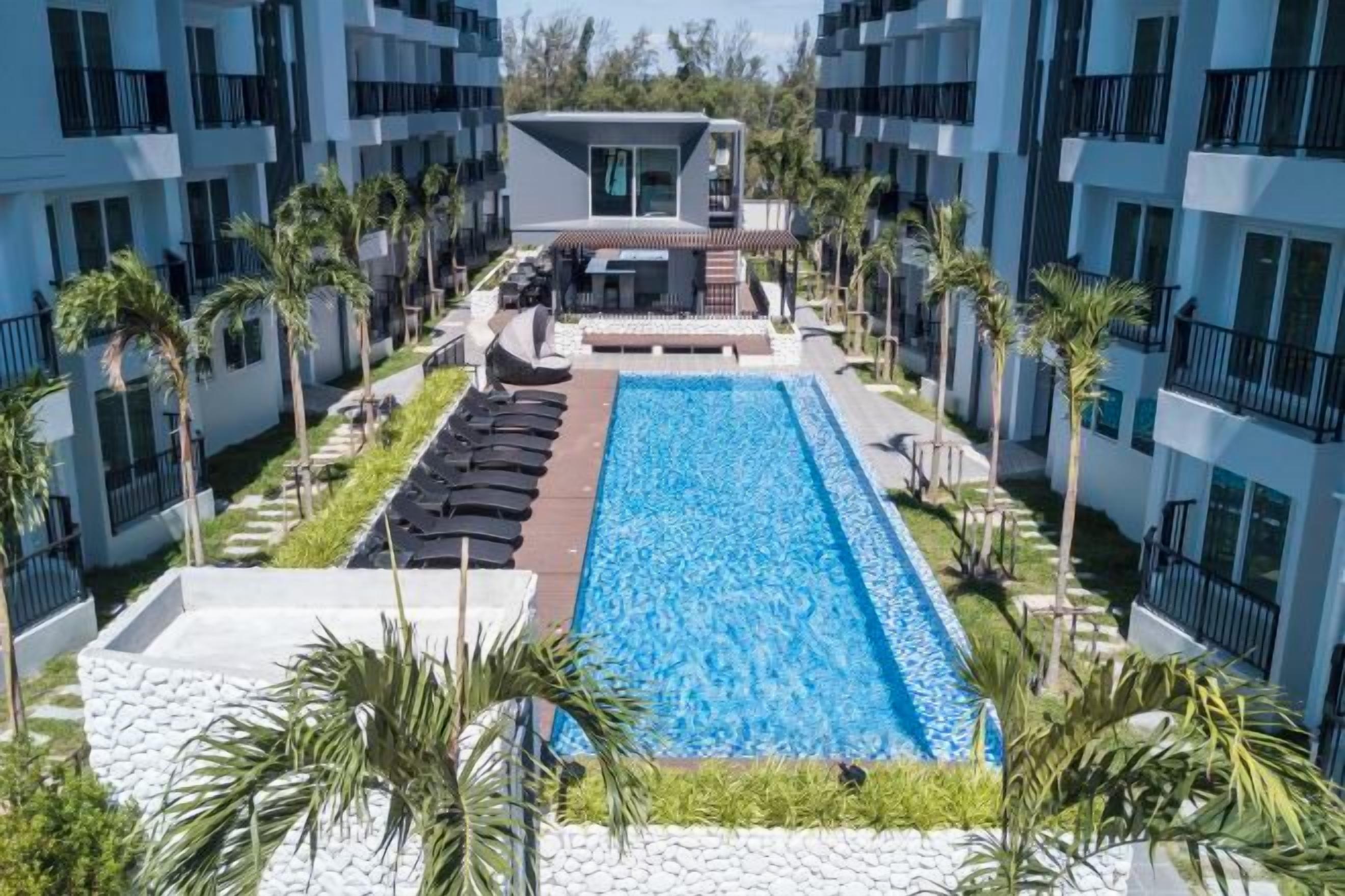 Una piscina rodeada de sillones de descanso y palmeras, con un edificio al fondo.