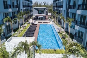 A swimming pool surrounded by lounge chairs and palm trees, with a building in the background. - Mantra Beach Condominium MaePhim - 2 (Klaeng)