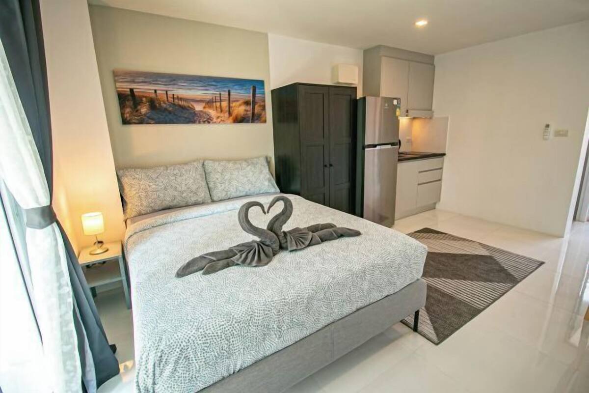A modern bedroom with a bed, a painting, a wardrobe, and a kitchenette.