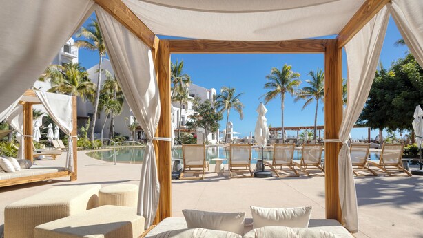 Eine Strandlounge mit bequemen Sitzgelegenheiten und Blick auf Pool und Palmen.