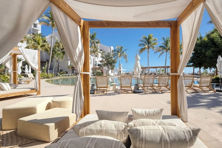 A beachside lounge area with cushioned seating and a view of the pool and palm trees.