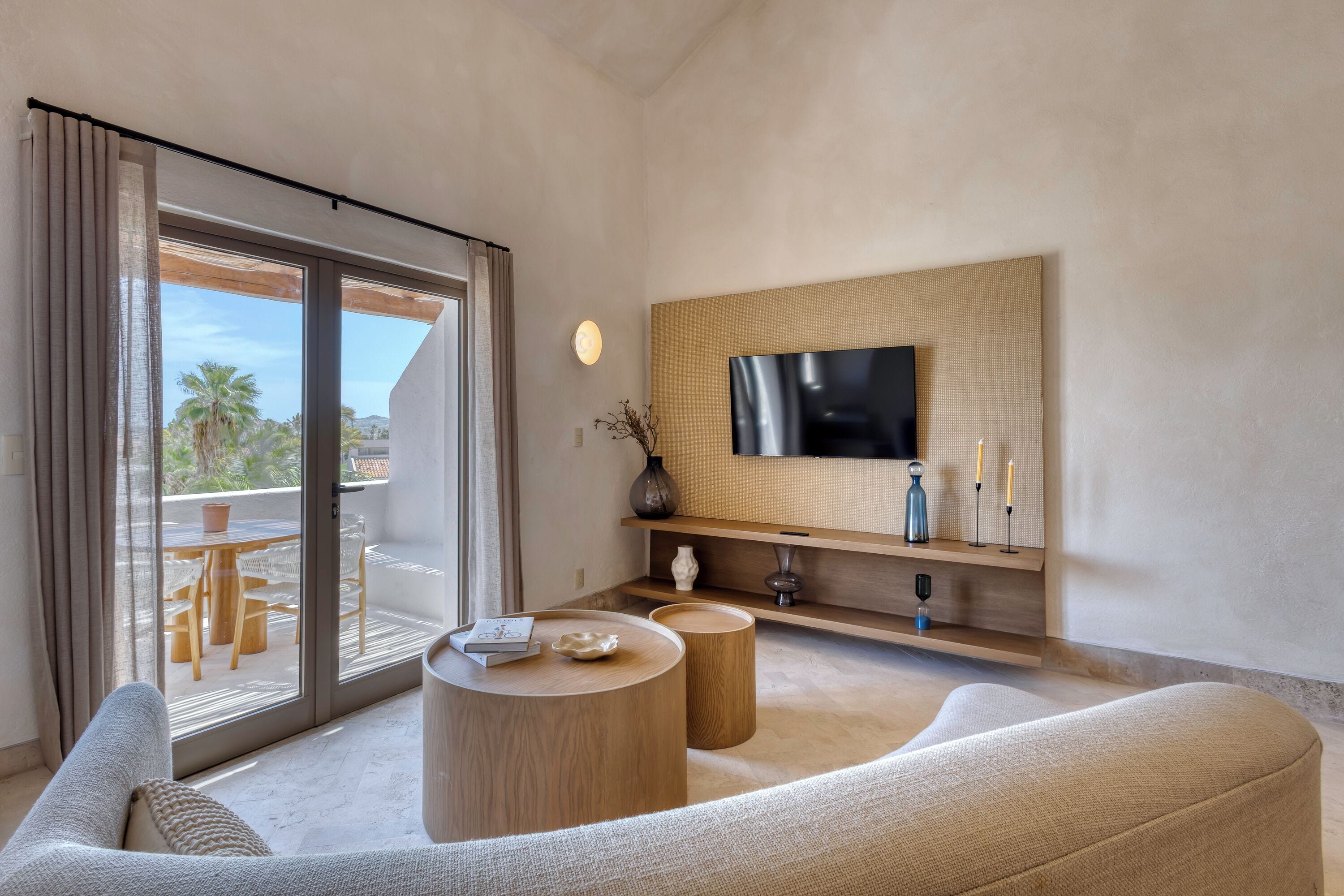 A modern living room with a large TV, wooden furniture, and a view of the outdoors.