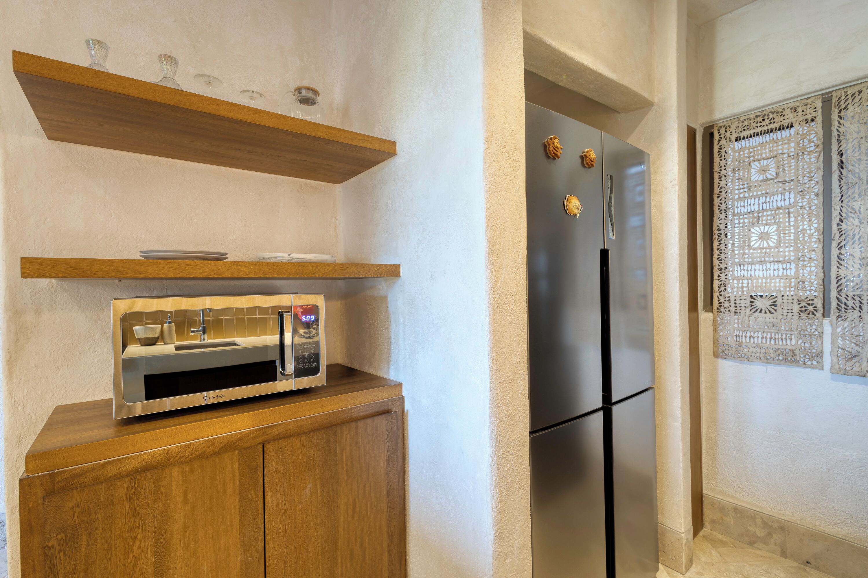 Una cocina con microondas integrado, un refrigerador de acero inoxidable y repisas de madera sobre la encimera.