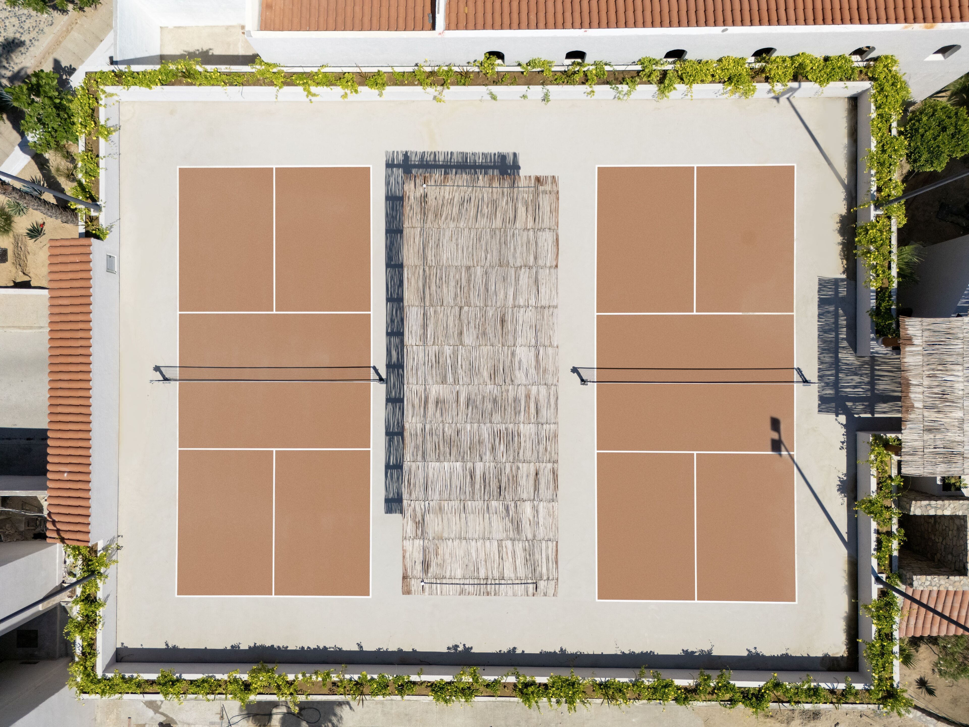 Vue aérienne d’un court de tennis entouré de verdure et bordé de bâtiments.
