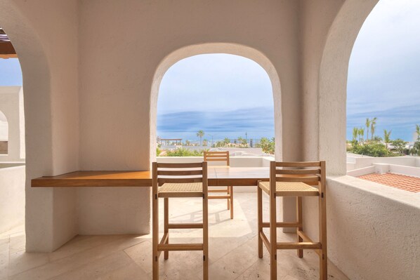 Una terraza con mesa y sillas, vista al mar y un edificio blanco con arcos.