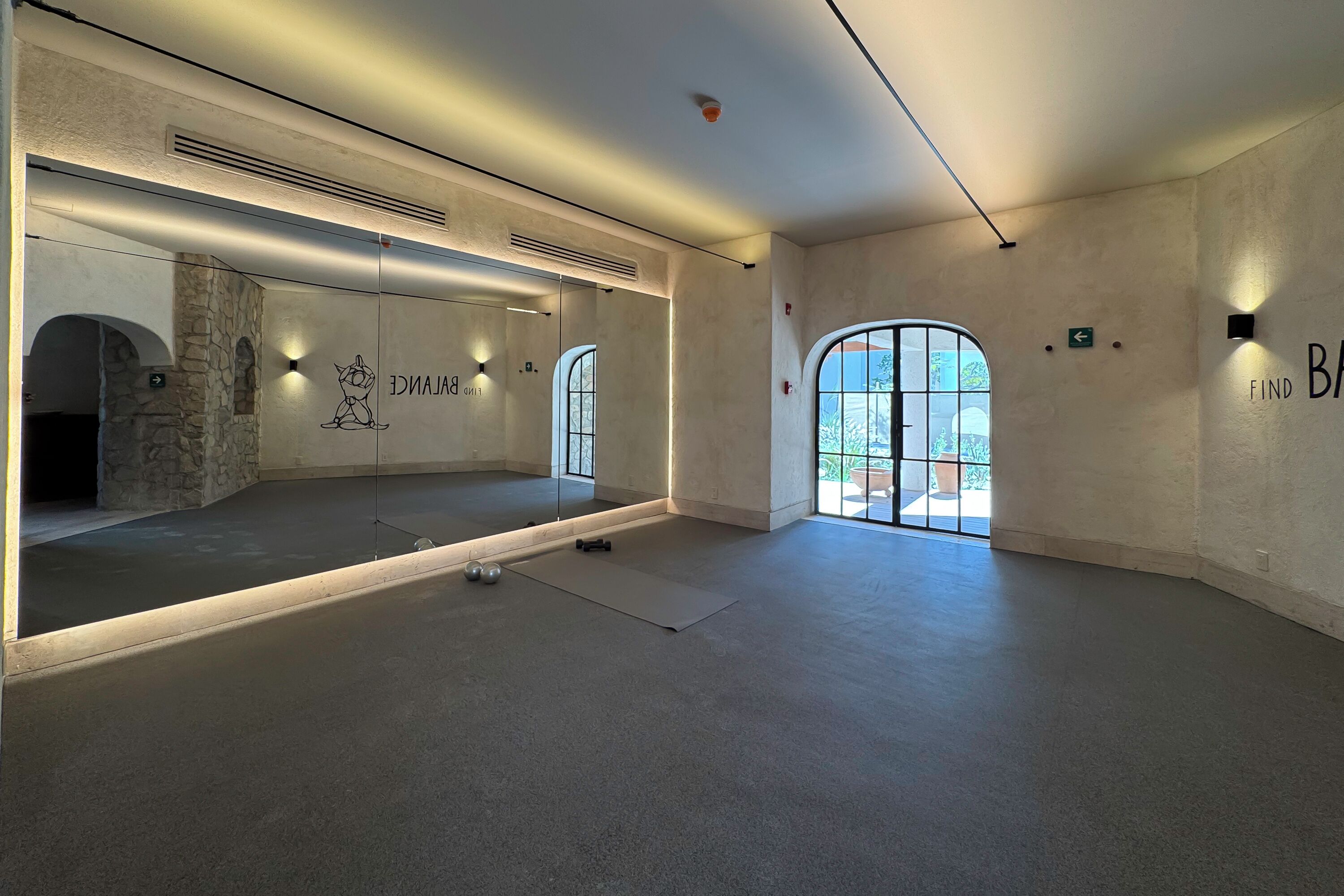 Une pièce spacieuse avec un grand miroir, un tapis de yoga et une paire d’haltères.