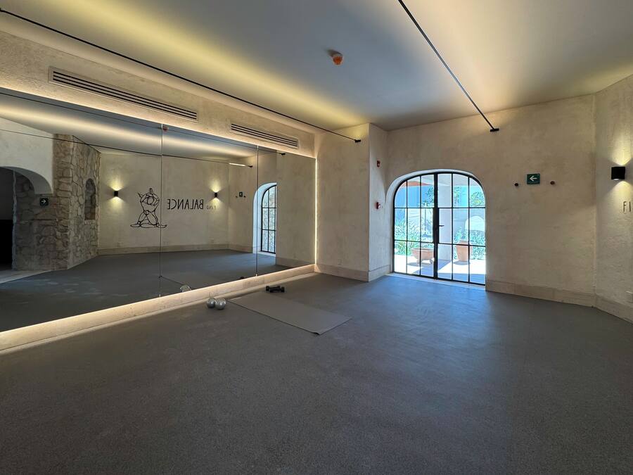 Une pièce spacieuse avec un grand miroir, un tapis de yoga et une paire d’haltères.