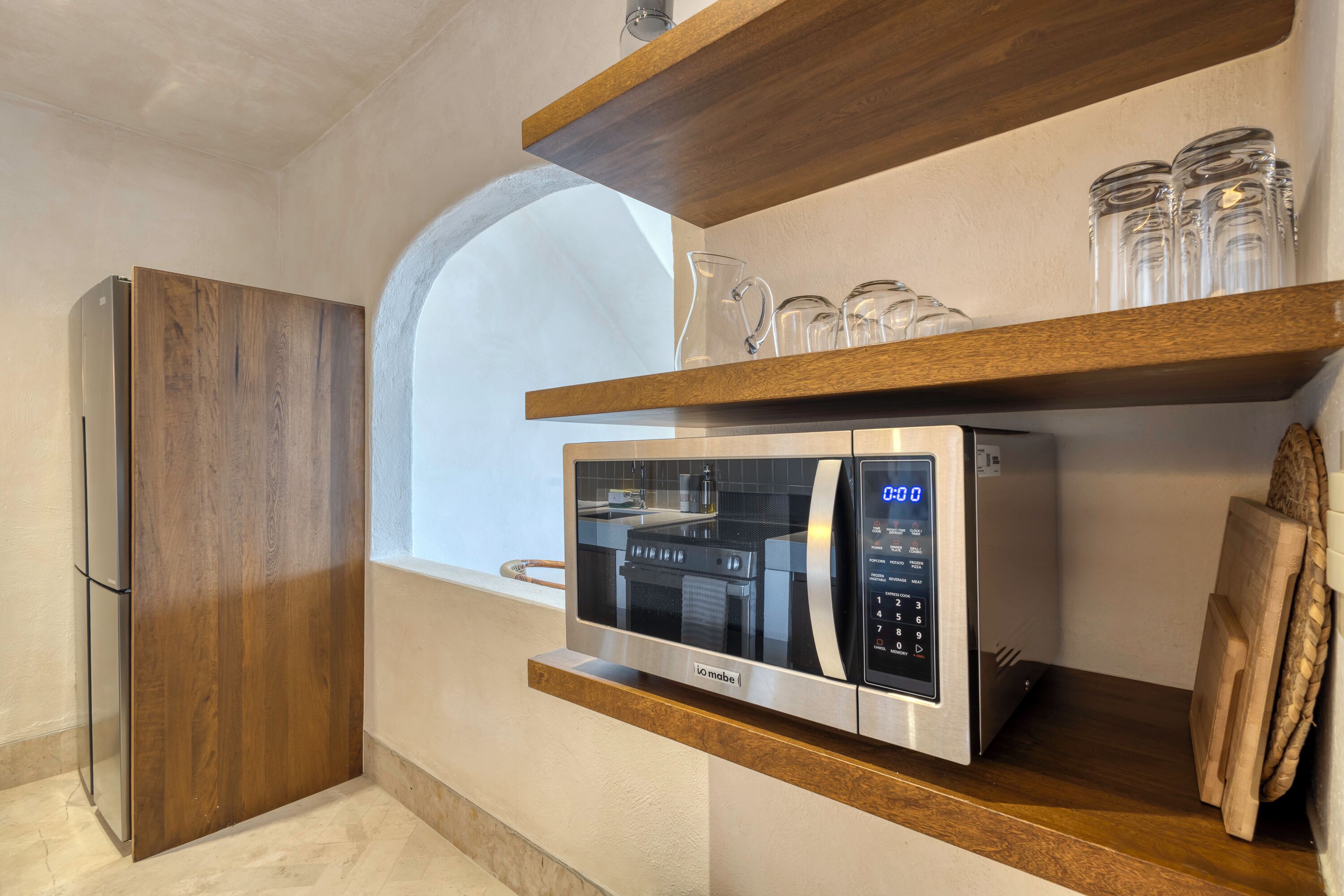 A kitchen with a built-in microwave, wooden shelves, and a refrigerator.