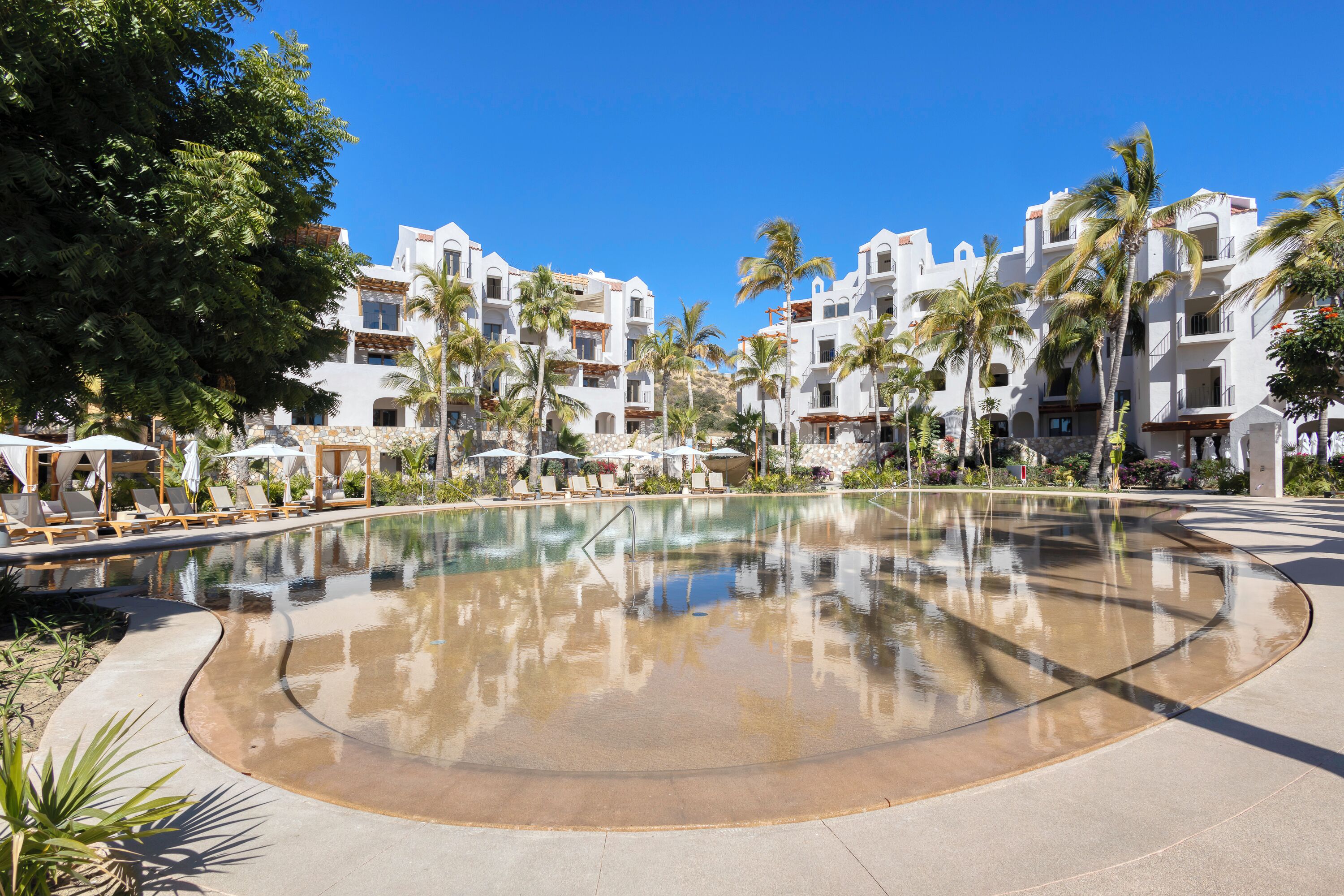 A resort with a large pool, palm trees, and white buildings with balconies.