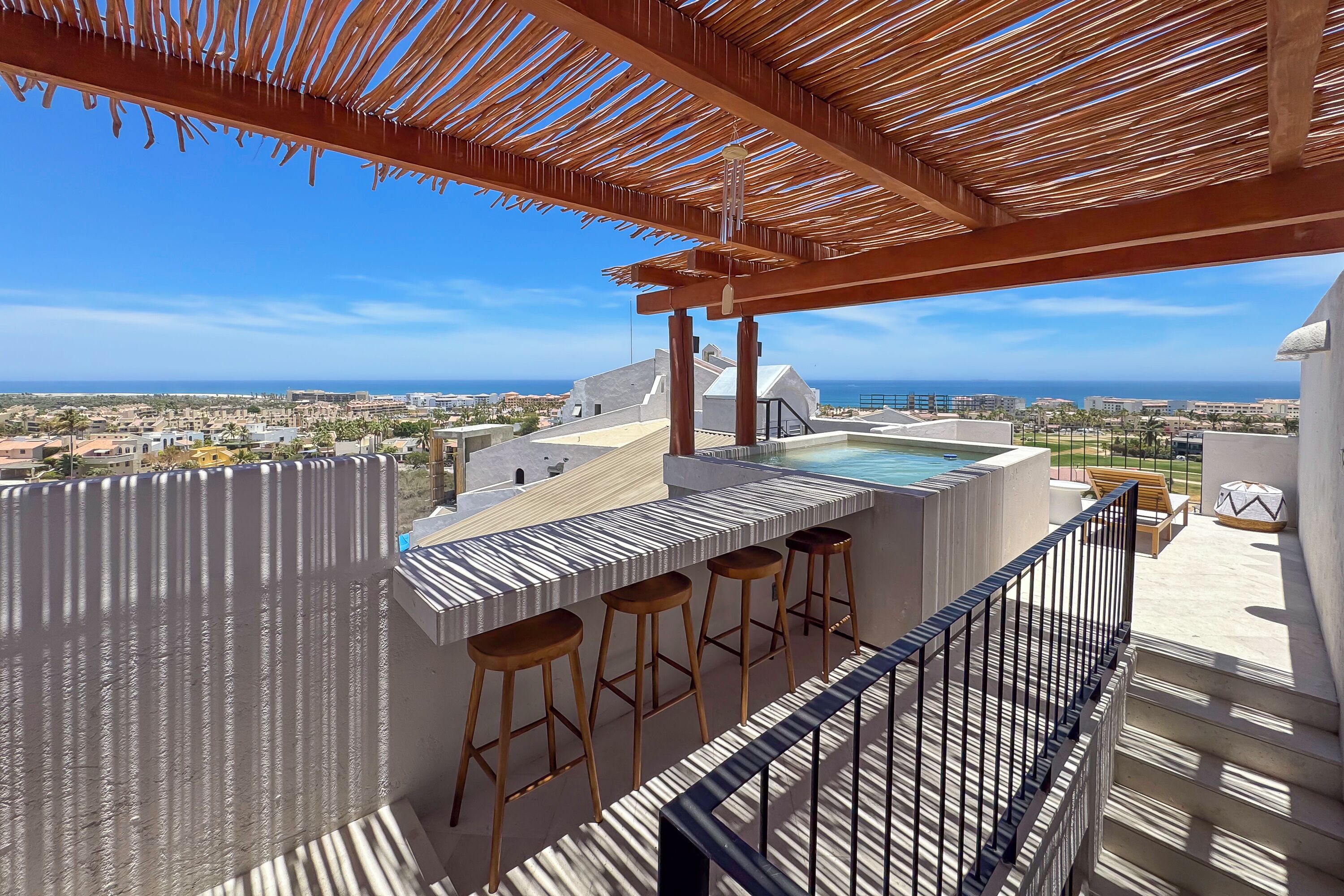 A rooftop bar with a pool, wooden stools, and a view of the city and ocean.