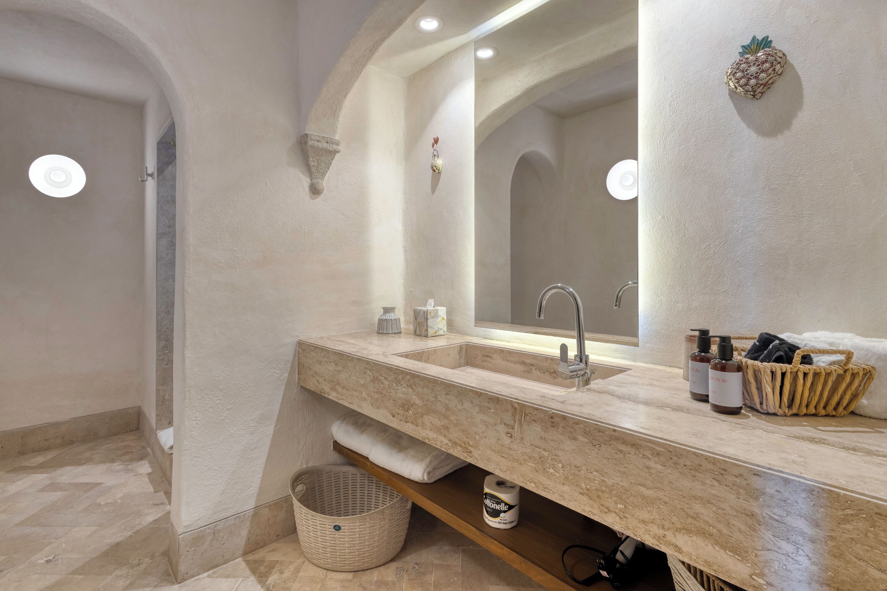 A modern bathroom with a marble sink, a large mirror, and a basket of toiletries.