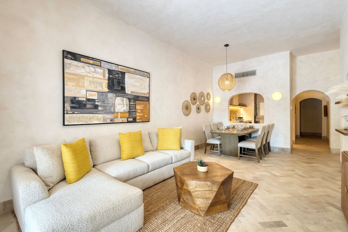 Una sala de estar con un sofá modular, una mesa de centro y una zona de comedor con sillas y una mesa.