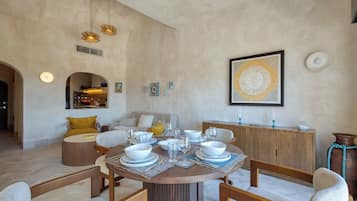 Zona pranzo con tavolo rotondo apparecchiato per sei, circondato da sedie di legno. Si nota un mobiletto in legno con oggetti decorativi e un quadro appeso alla parete.
