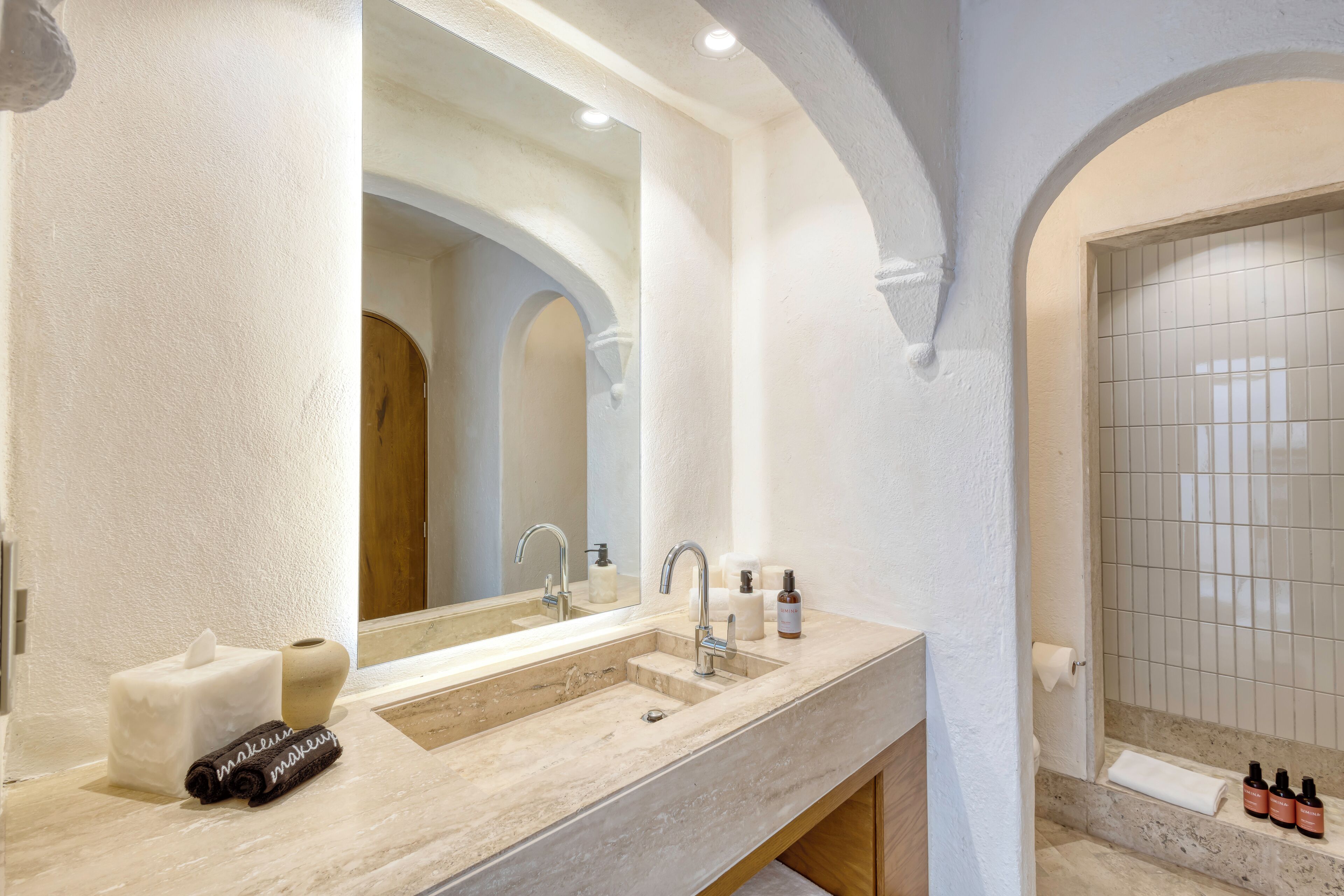 A bathroom with a large mirror, two sinks, a towel rack, and a shower area.