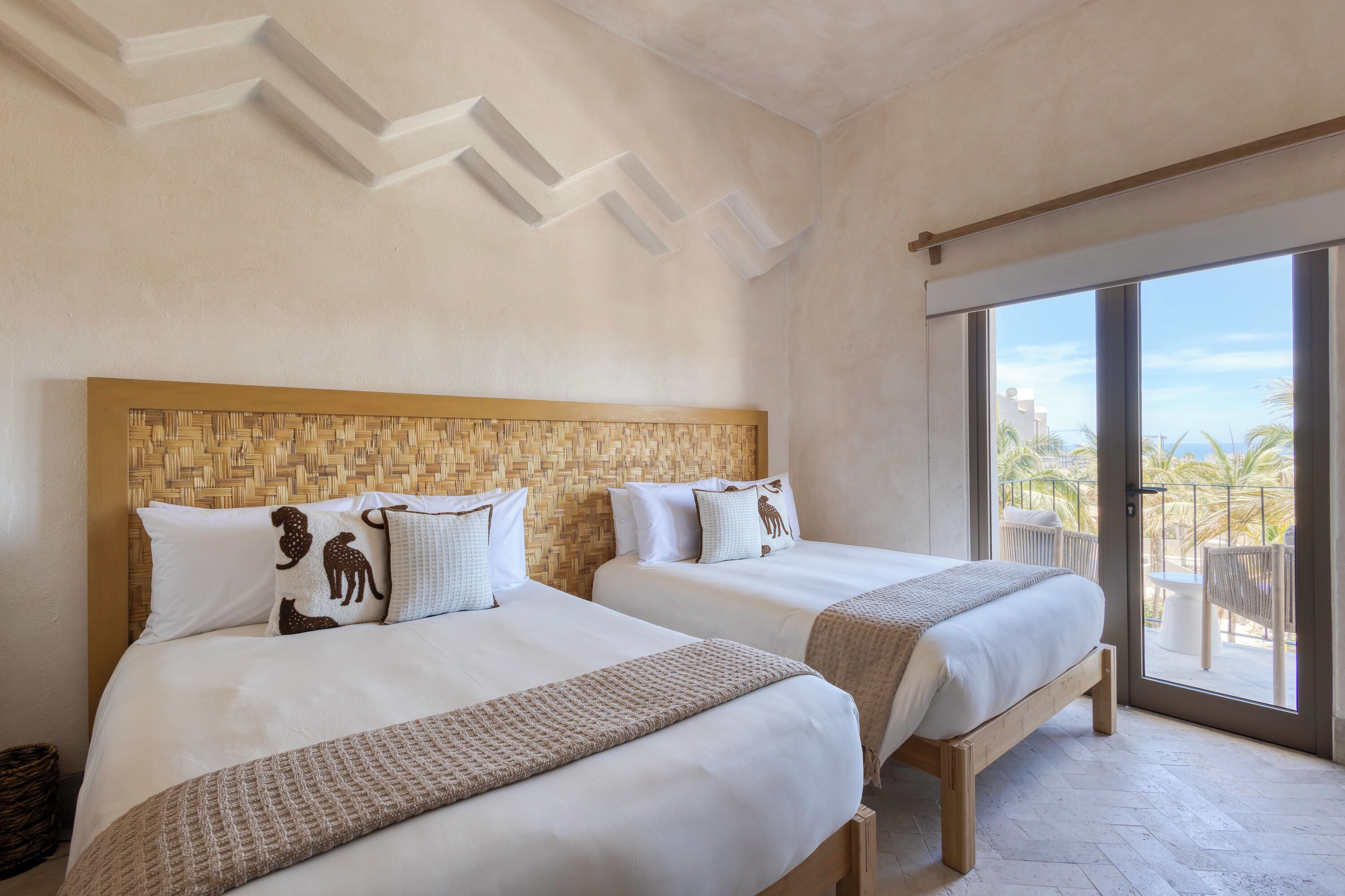 A hotel room with two beds, a woven headboard, and a balcony with a view.
