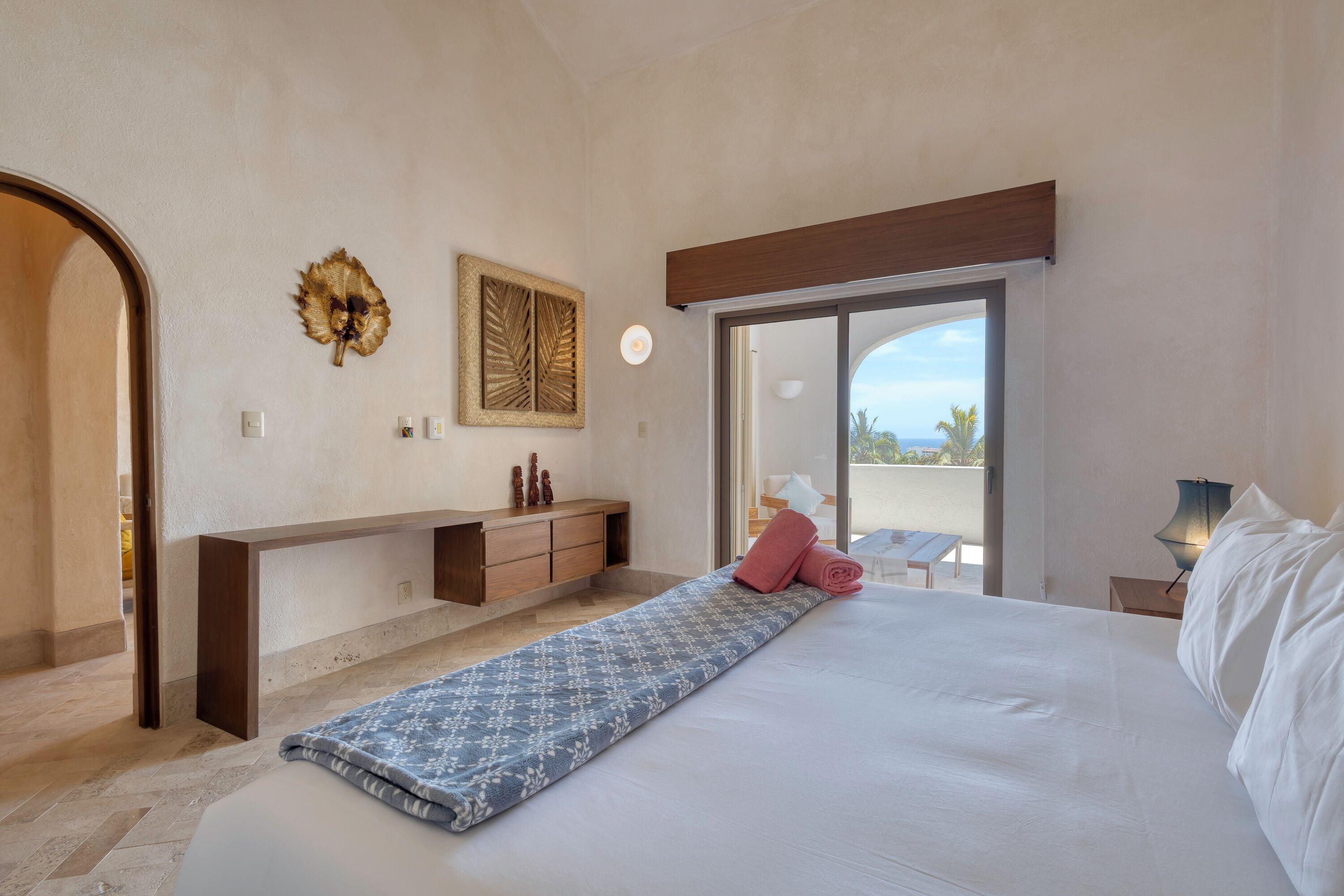 A bedroom with a bed, a bench, a desk, and a view of the outdoors.