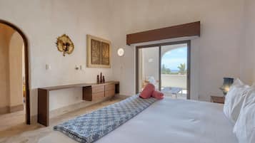 A bedroom with a bed, a bench, a desk, and a view of the outdoors.