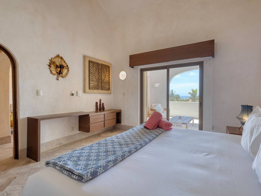 A bedroom with a bed, a bench, a desk, and a view of the outdoors.