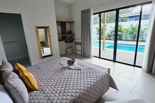 Un dormitorio con una cama grande, baño y vista a una piscina.