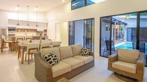 A modern living room with a sofa and armchairs, a dining area with chairs, and a kitchen in the background.