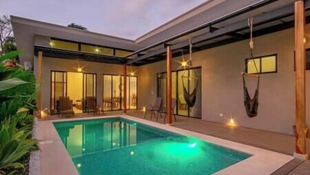 A modern house with a swimming pool, large windows, and a hammock.